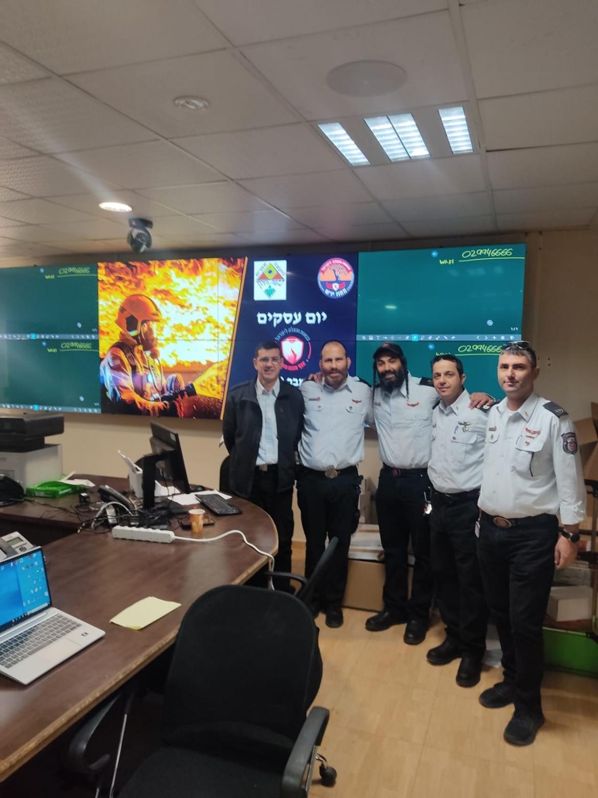 אנשי כיבוי והצלה עומדים בחדר ישיבות ליד מסכים עם הודעות לבעלי העסקים