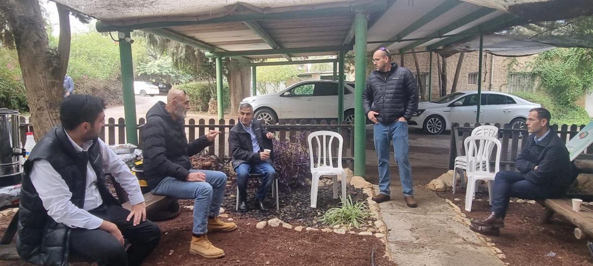 חכ סעדה, ראש המועצה, יור הועדה החקלאית יושבים בחצר מתחת לסככה ומדברים. ברקע מכוניות חונות
