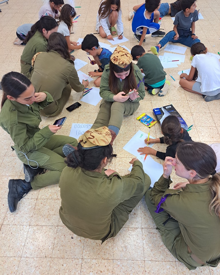 חיילות וילדים יושבים על הרצפה ומציירים כרטיסי ברכה