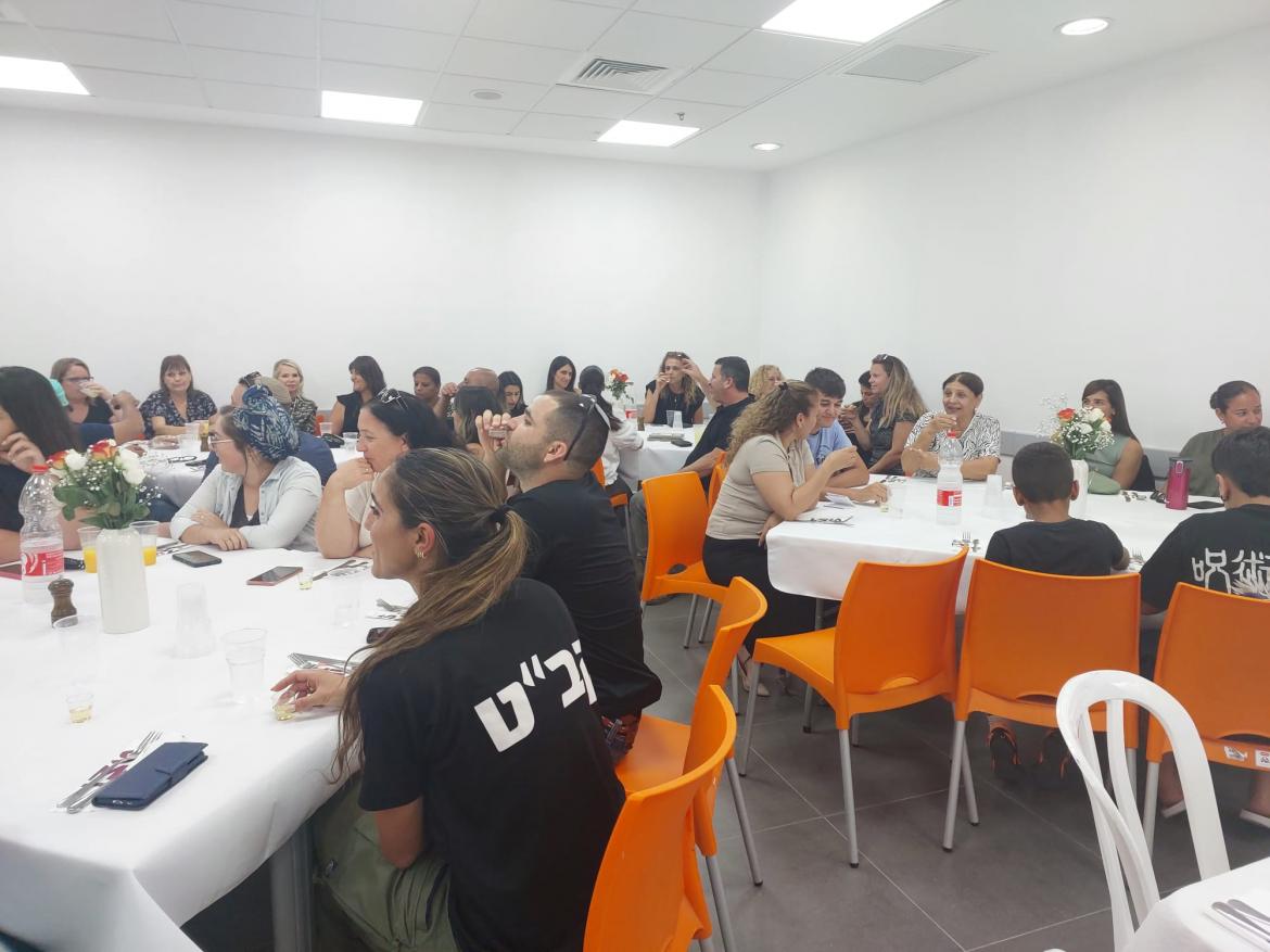 עובדי המועצה יושבים מסביב לשולחנות עם מפות לבנות