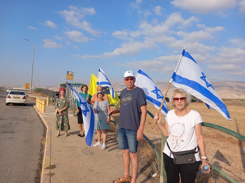 אנשים עומדים עם דגלי ישראל לצידי הכביש