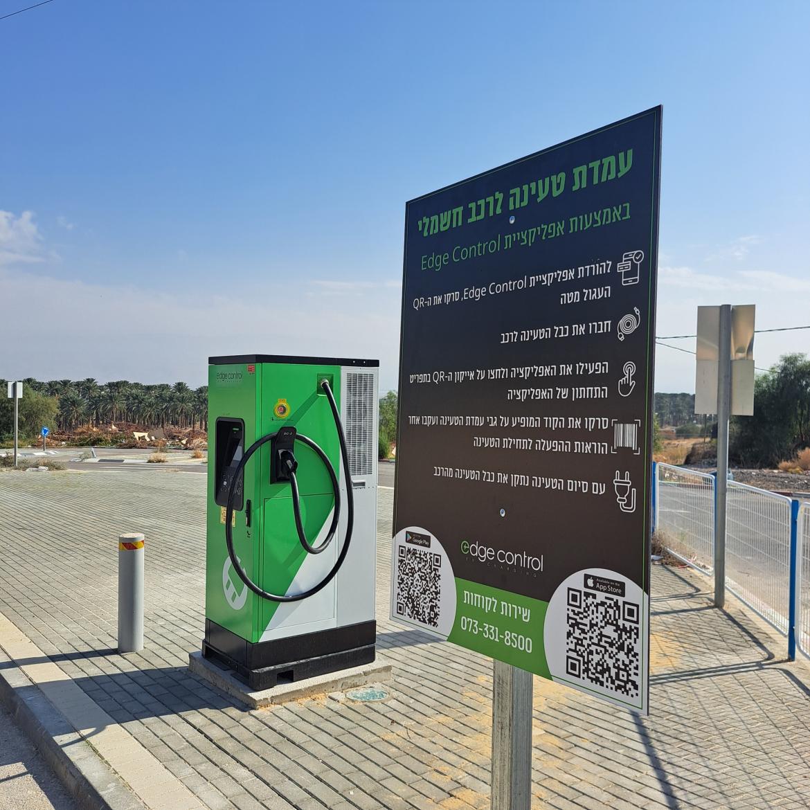 שלט עם הנחיות לטעינה לרכב חשמלי שמוצב מעל מדרכה ולידו עמדת הטעינה