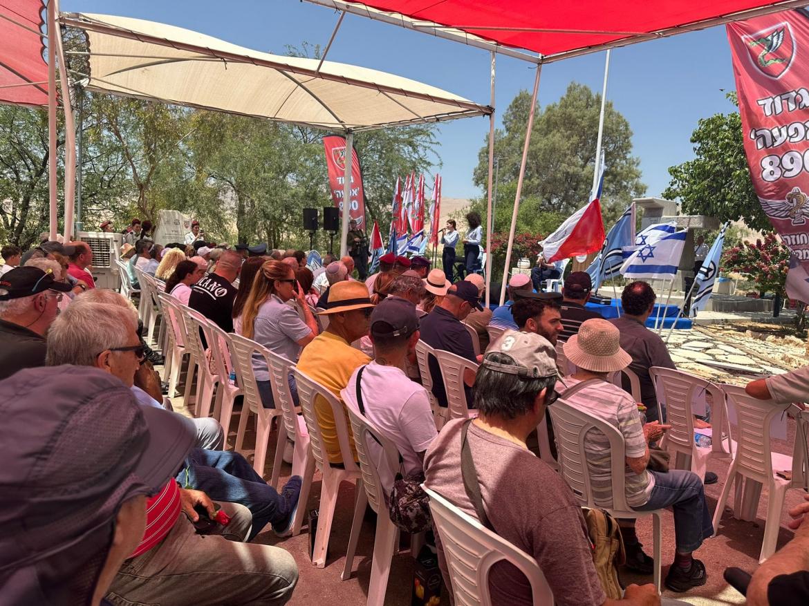 הקהל יושב בטכס מתחת לסככות ומקשיב לנאום